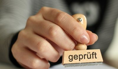 Hand die einen Stempel hält, auf dem geprüft steht