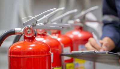 Feuerlöscher aufgereiht, man sieht eine Hand, die auf einem Klemmbrett etwas einträgt